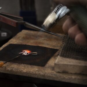 Goldsmith holding a torch soldering a piece of silver on a soldering board or soldering block