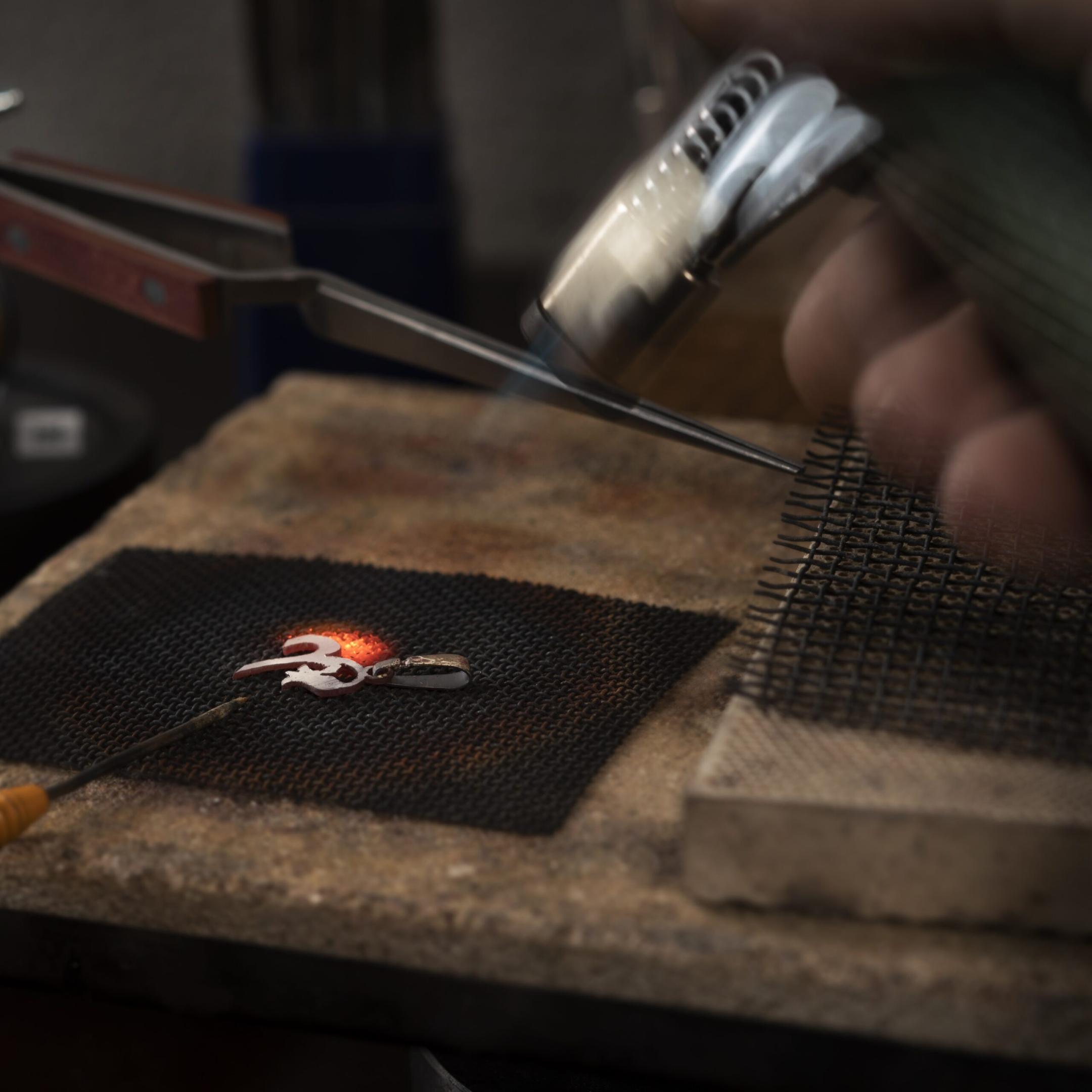 Goldsmith holding a torch soldering a piece of silver on a soldering board or soldering block